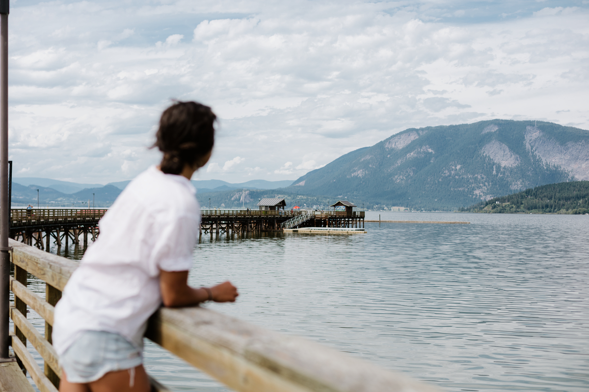 A woman looks out from the Salmon Arm Wharf to the water. She is wearing a white t-shirt and shorts.