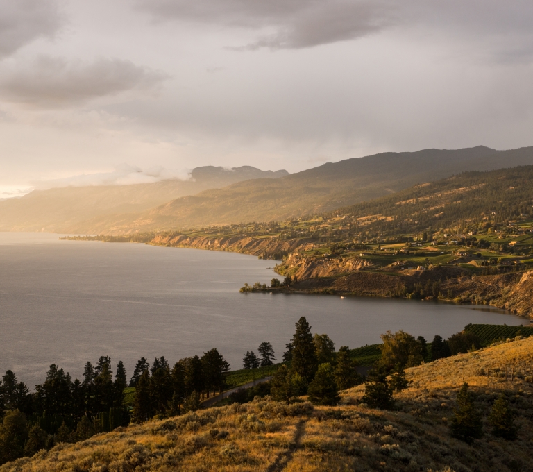 Sunset over Okanagan Lake and Naramata from Munson Mountain. The hills are gently sloped down towards the lake with vineyards and farmlands.