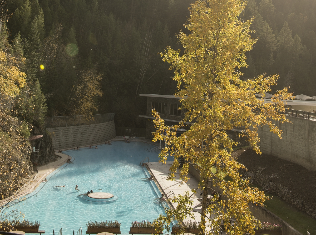 An overview shot of Radium Hot Springs pools. People are in the pools. The leaves on the trees closest are turning yellow.