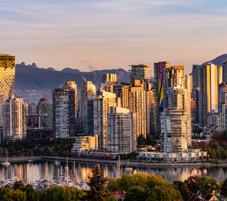 Aerial photo of Vancouver skyline as the sunsets. The light reflects off the downtown skyscrapers and the mountains are seen in the distance.