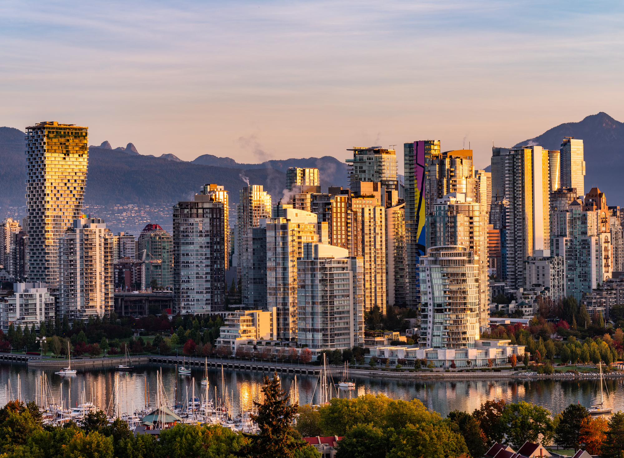 Aerial photo of Vancouver skyline as the sunsets. The light reflects off the downtown skyscrapers and the mountains are seen in the distance.