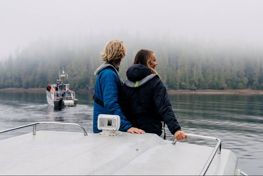 A couple standing on the back of a boat looking out at the water on a guided black bear watching tour.