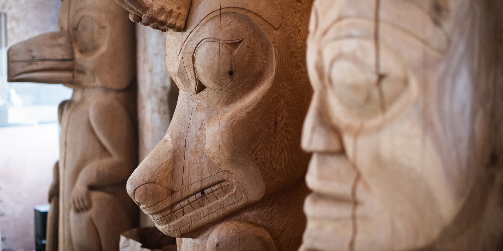 Close-up view of the middle section of three totem poles. In the frame are a human face, a wolf, and a raven.
