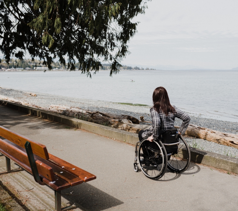 Woman in a wheelchair on a paved path along the Qualicum Beach waterfront | Lexa Bergen