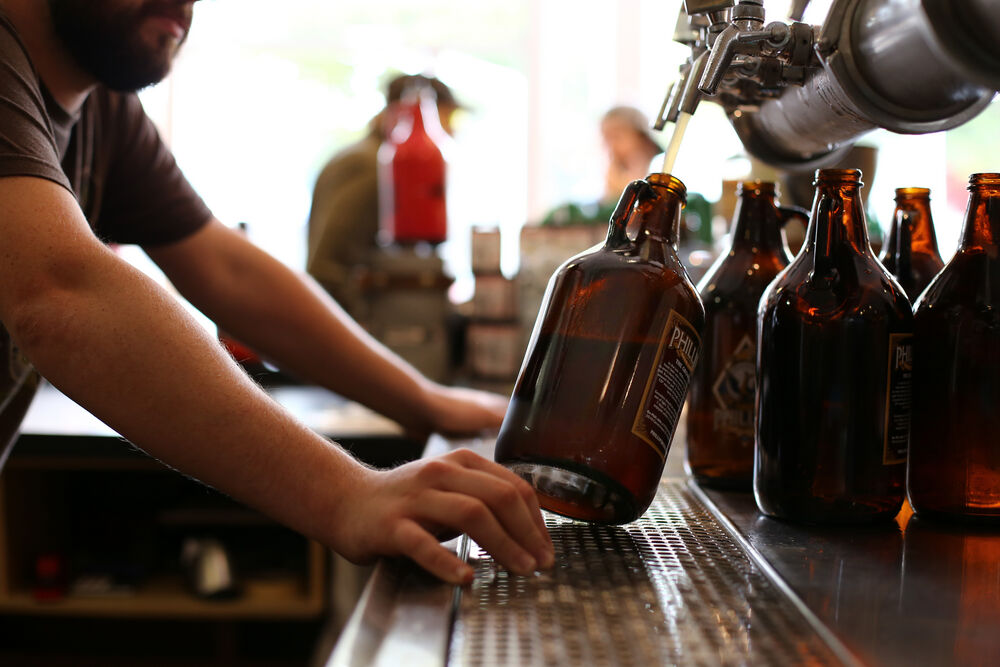 a growler is being held on a 45-degree angle as it is being filled. Empty growlers sit to its right.
