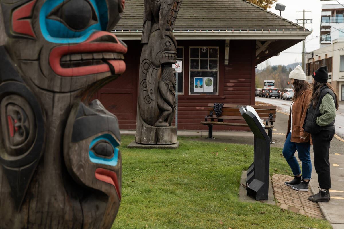Two people reading interpretive signage and viewing Indigenous totem poles on the Duncan Totem Walk.