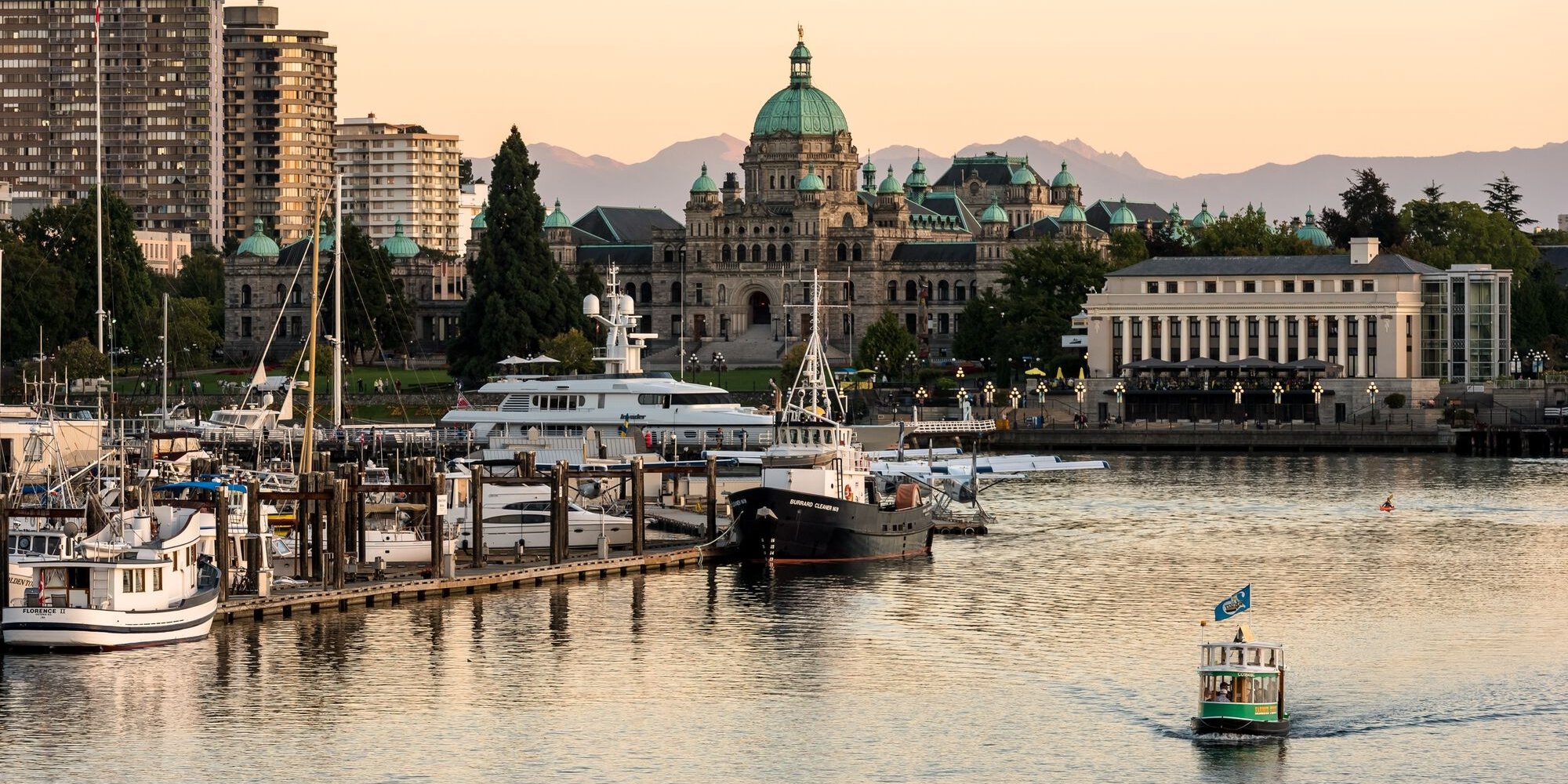 A water taxi moves through the water on the right with a marina on the left of the frame. Buildings are visible in the background, including the intricate legislature.