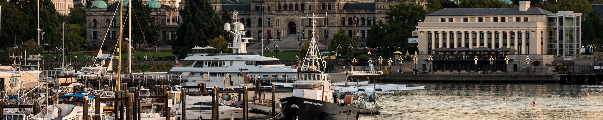 A water taxi moves through the water on the right with a marina on the left of the frame. Buildings are visible in the background, including the intricate legislature.