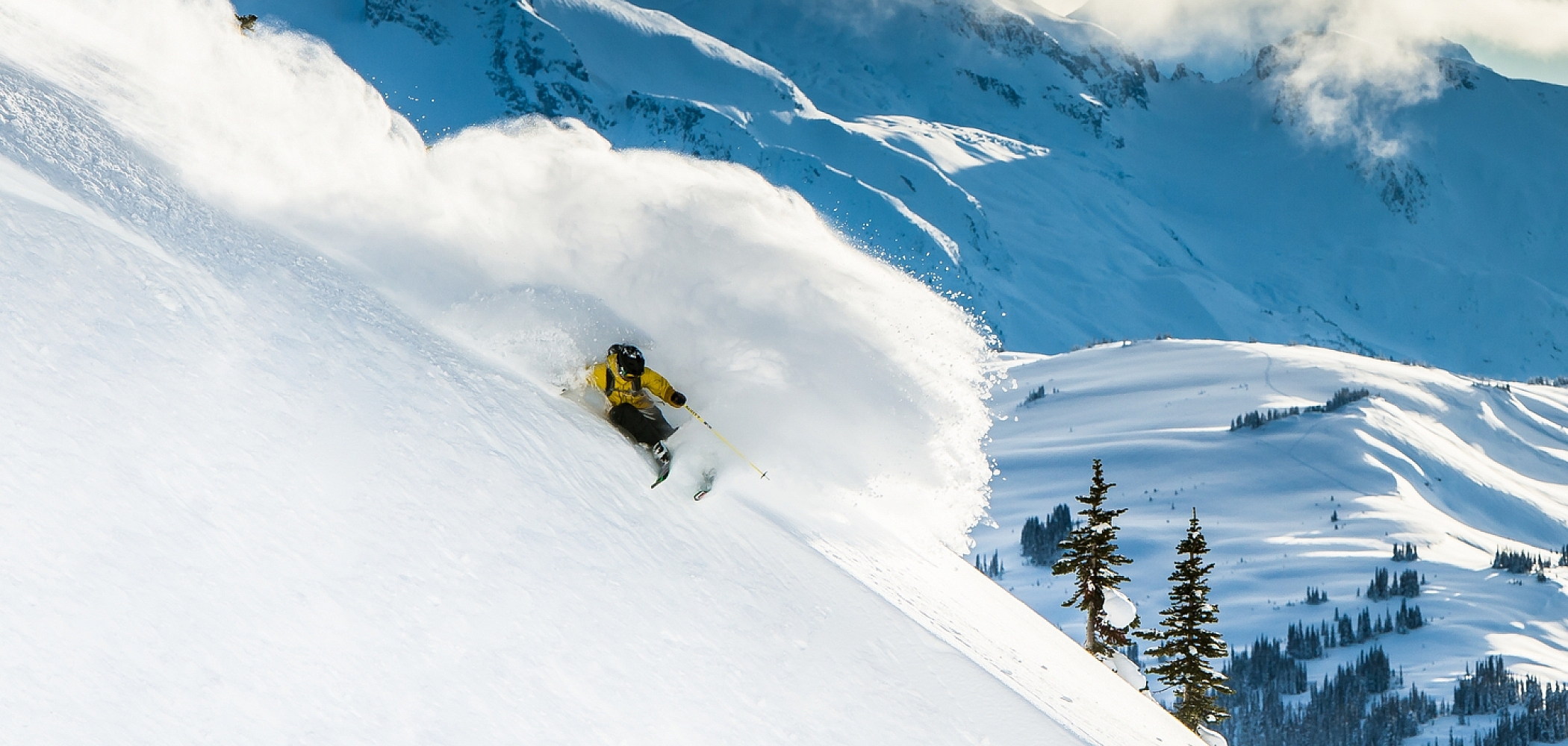 A skier glides through deep powder in Whistler with the Coast Mountain range in the backdrop.