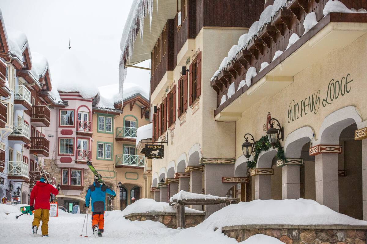 Skiers with gear over their shoulders walk through the snow-covered village at Sun Peaks Resort.