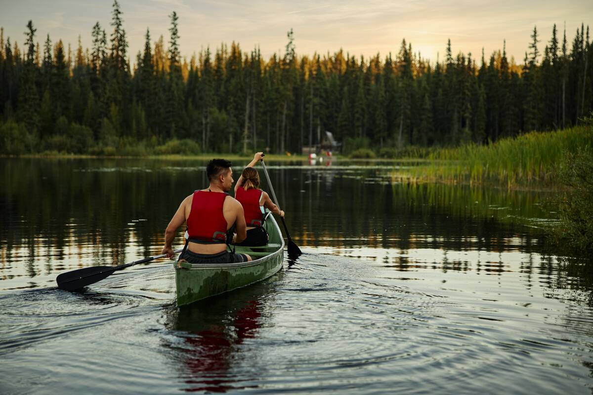 A couple canoeing at Chute Lake during sunset. Chute Lake Lodge in the background