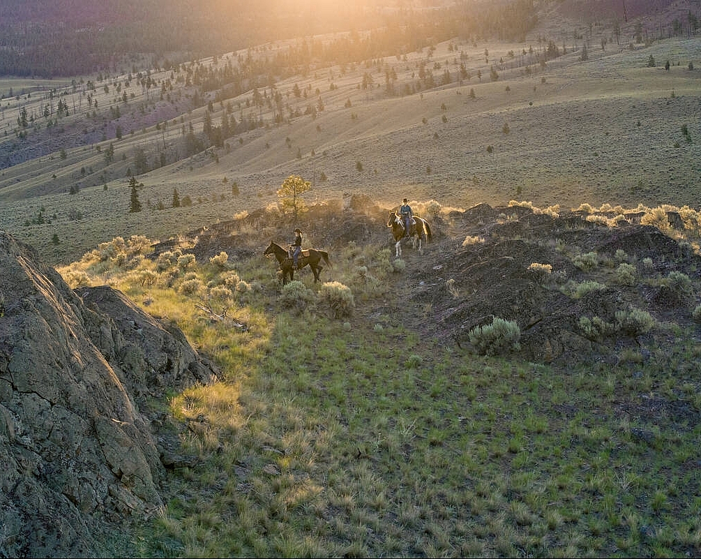 Two people on horseback riding through the sagebrush-covered hills.