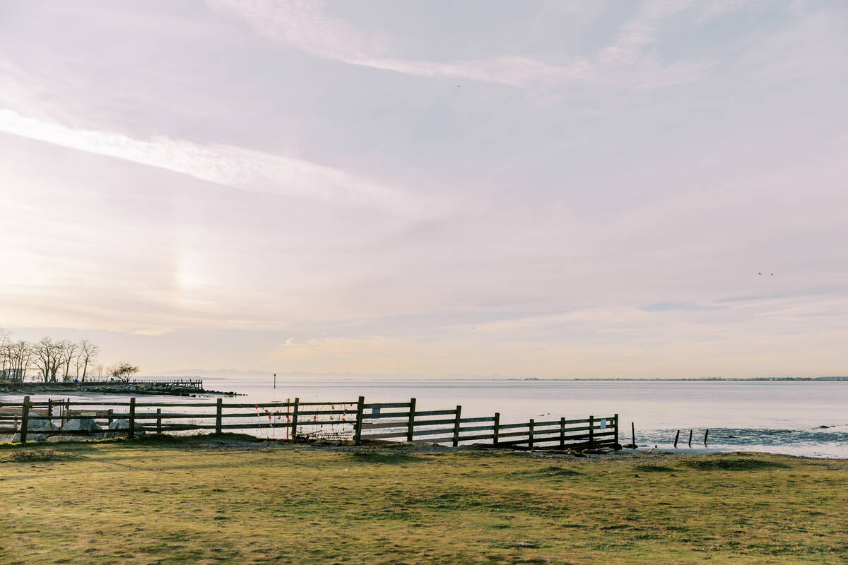A grassy field sits in the foreground with a wooden fence on the left of the frame that leads to the ocean's edge