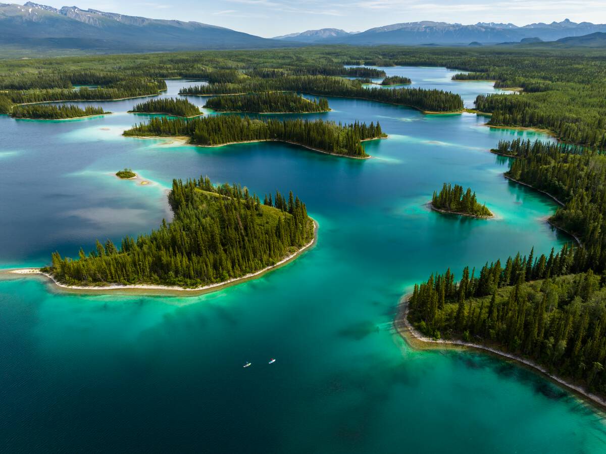 An aerial view of people paddling vibrant turquoise lake waters dotted by small islands.