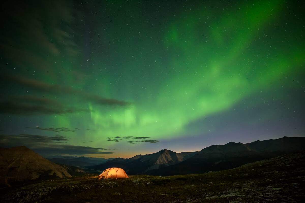 An illuminated tent under the Northern Lights.